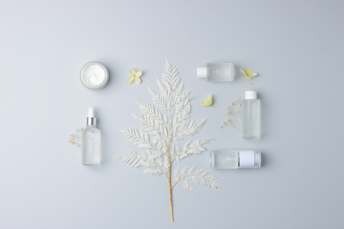 Cosmetic composition with cosmetic skin care products and flowers on grey background. Flat lay, copy space